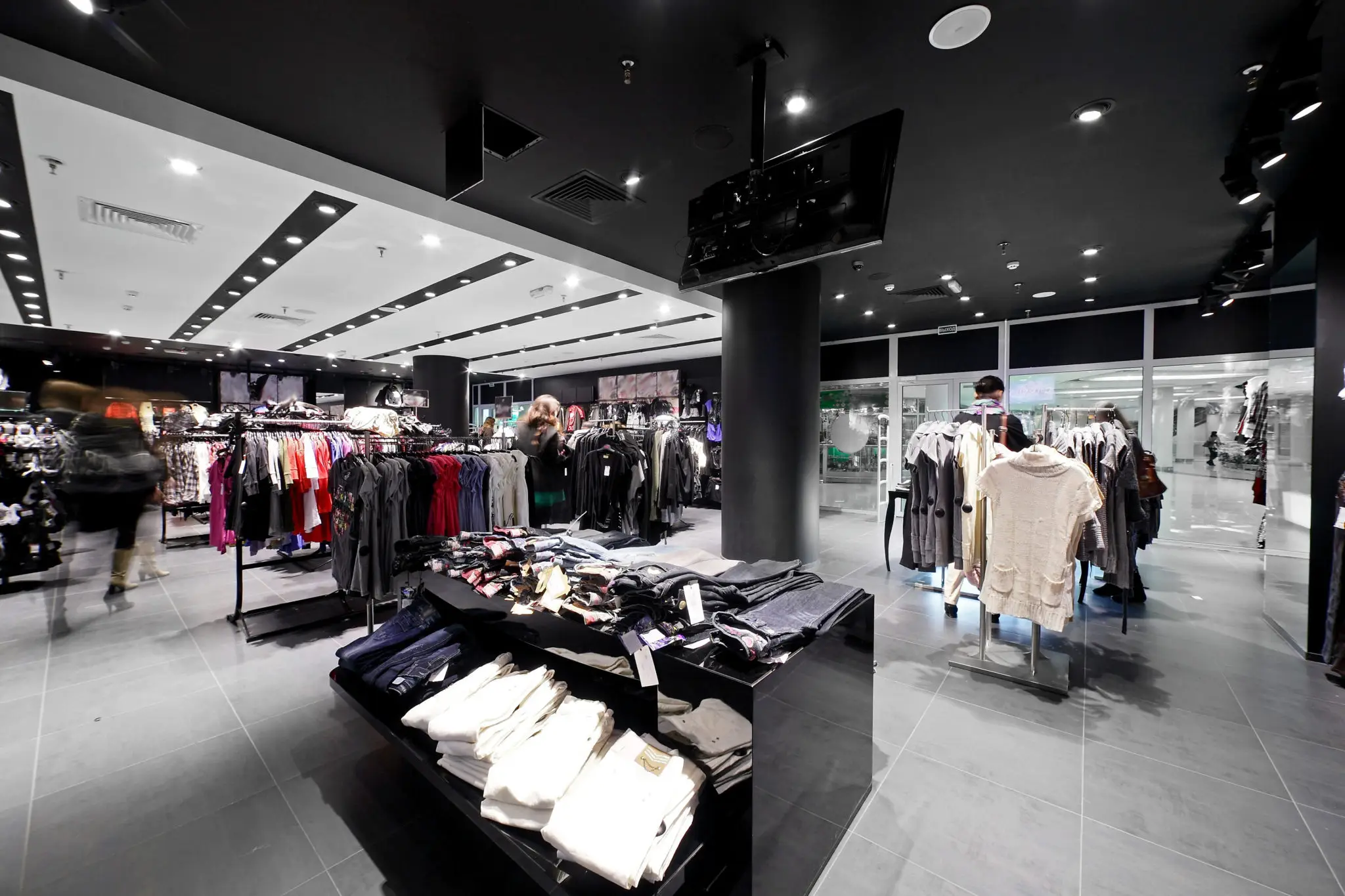 A bright retail clothing store with light floors and dark fixtures